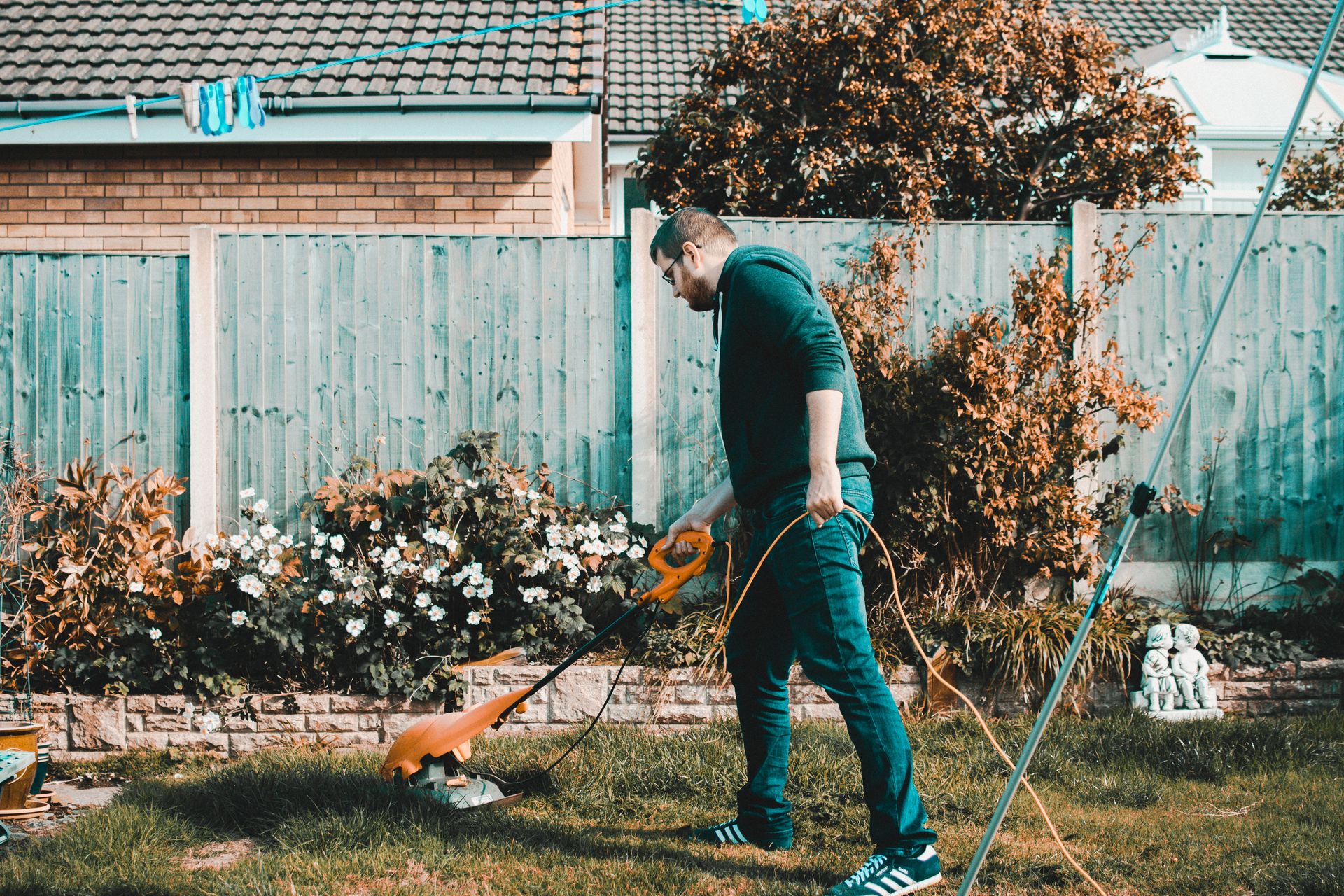 String trimming along a fence line and flower bed border in a backyard